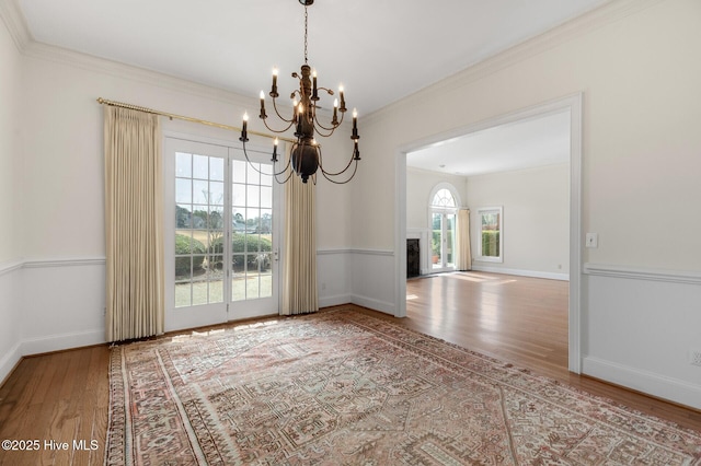 unfurnished dining area with a fireplace, baseboards, crown molding, and wood finished floors