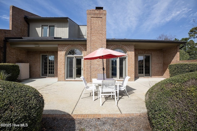 rear view of property featuring brick siding, a chimney, and a patio