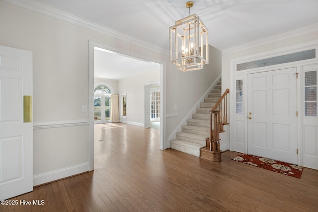 foyer entrance with a notable chandelier, ornamental molding, wood finished floors, baseboards, and stairs