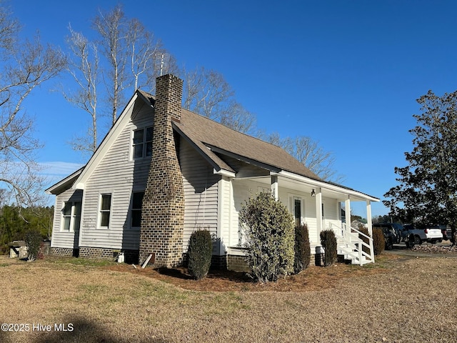 view of side of home with a yard, a porch, and a chimney