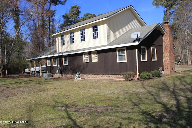 view of side of home with cooling unit, a yard, and a chimney