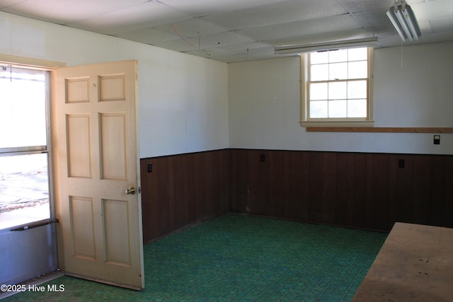 spare room with a wainscoted wall, wood walls, and a drop ceiling