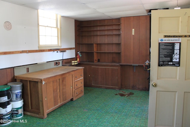 kitchen featuring open shelves, wood walls, a drop ceiling, and brown cabinets