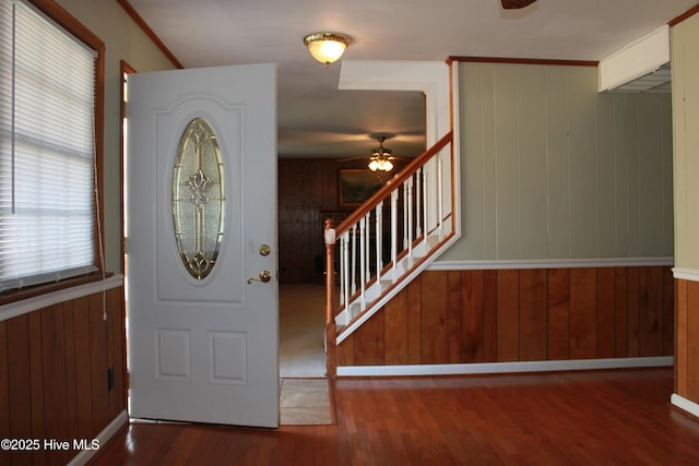 entrance foyer with ceiling fan, wood walls, wood finished floors, stairway, and crown molding