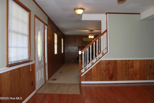 entryway with ornamental molding, stairway, wooden walls, and wood finished floors