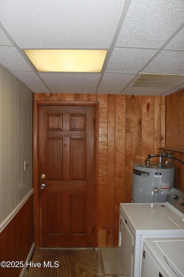 clothes washing area with laundry area, water heater, wood walls, and washing machine and clothes dryer