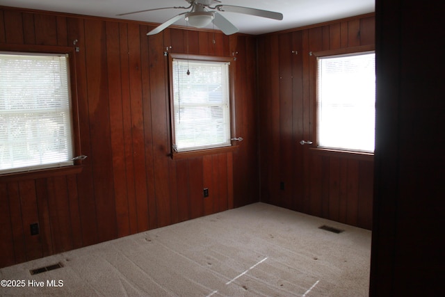 carpeted spare room featuring visible vents, a wealth of natural light, and wooden walls