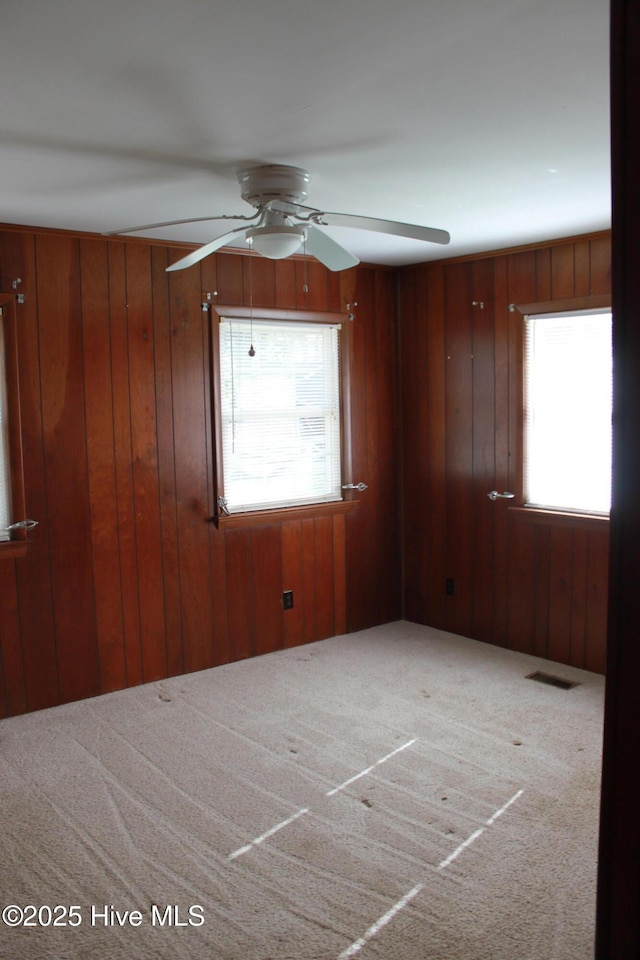 carpeted empty room with wood walls, visible vents, and a ceiling fan