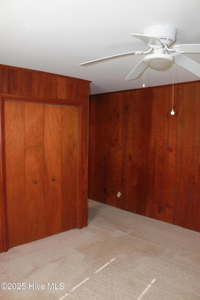 interior space with ceiling fan, wood walls, a closet, and carpet flooring