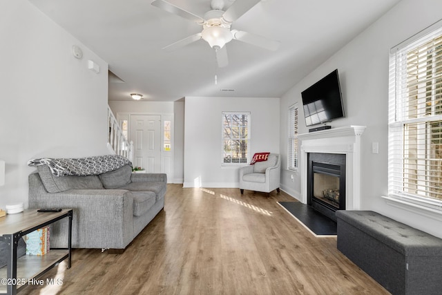 living area with ceiling fan, baseboards, wood finished floors, and a glass covered fireplace