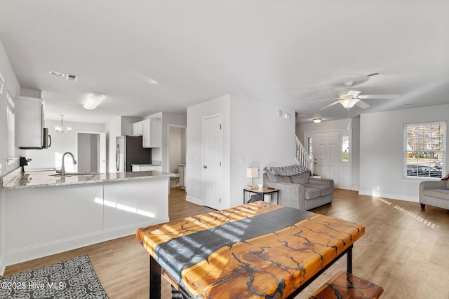 dining area featuring visible vents, ceiling fan with notable chandelier, stairway, light wood finished floors, and baseboards