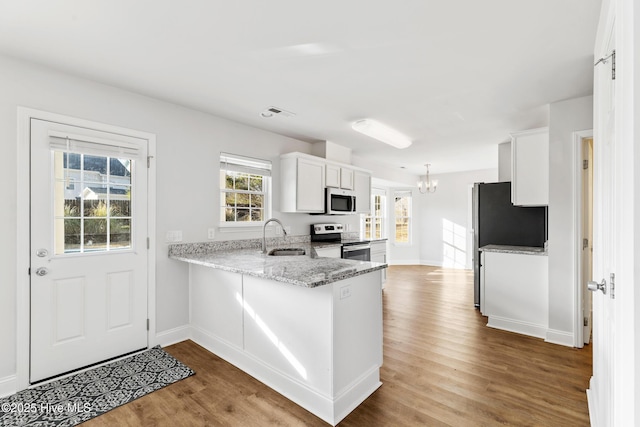 kitchen with wood finished floors, stainless steel electric stove, a sink, white cabinets, and a chandelier