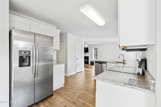 kitchen featuring light stone counters, stainless steel appliances, light wood-style floors, white cabinetry, and a sink