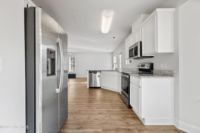 kitchen featuring white cabinets, light wood finished floors, light stone countertops, and appliances with stainless steel finishes