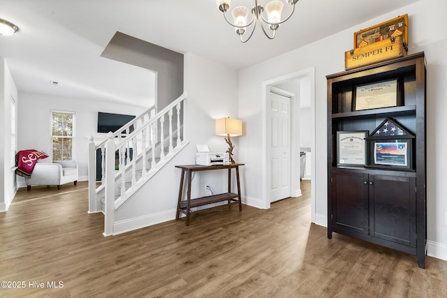 foyer with stairs, an inviting chandelier, and wood finished floors