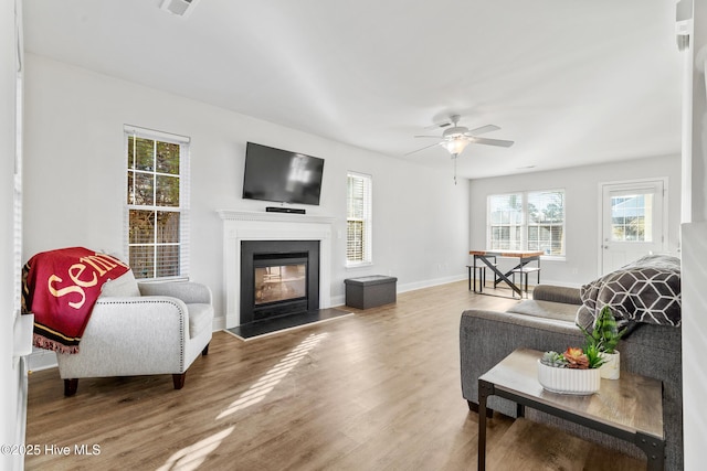 living area with ceiling fan, baseboards, a glass covered fireplace, and wood finished floors