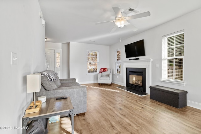 living area with a ceiling fan, wood finished floors, visible vents, baseboards, and a fireplace with flush hearth