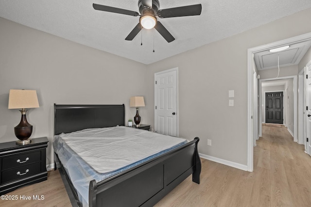 bedroom with a textured ceiling, light wood-style flooring, attic access, and baseboards