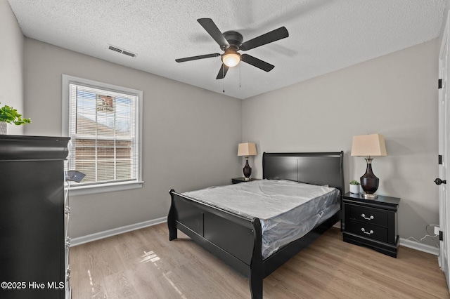 bedroom featuring a textured ceiling, wood finished floors, a ceiling fan, visible vents, and baseboards