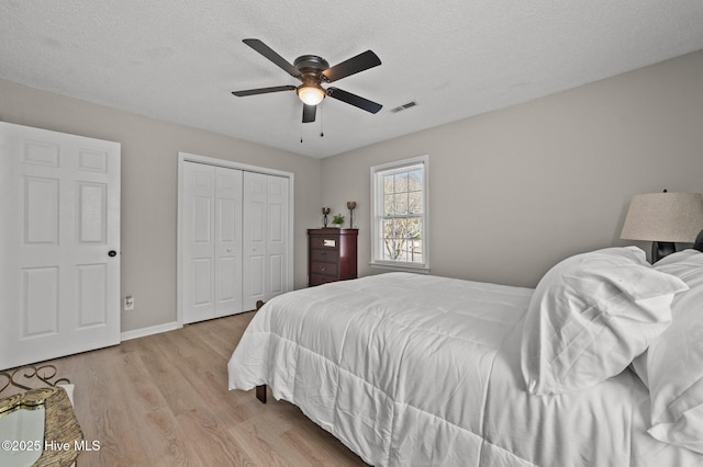 bedroom with a textured ceiling, light wood-style flooring, a closet, and visible vents