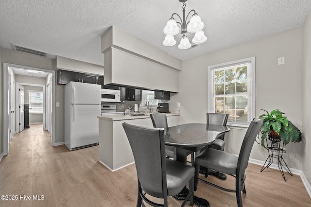 dining area with baseboards, visible vents, an inviting chandelier, a textured ceiling, and light wood-style floors