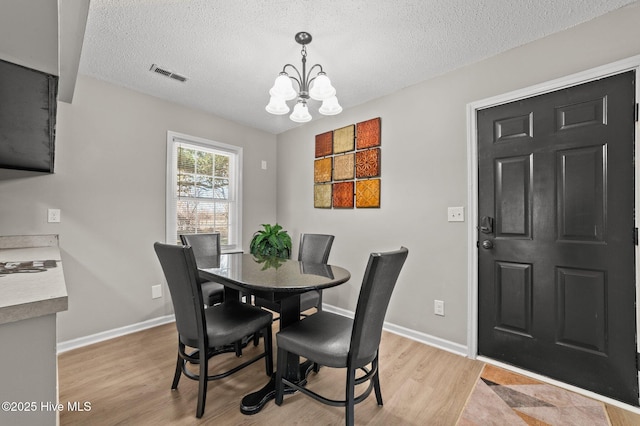 dining room with a notable chandelier, visible vents, a textured ceiling, light wood-type flooring, and baseboards