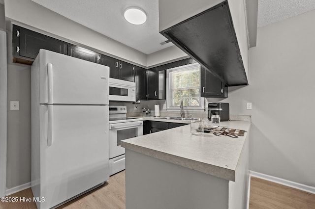 kitchen with a peninsula, white appliances, light countertops, and dark cabinets