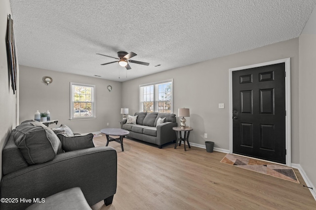 living room with light wood finished floors, a textured ceiling, baseboards, and a ceiling fan