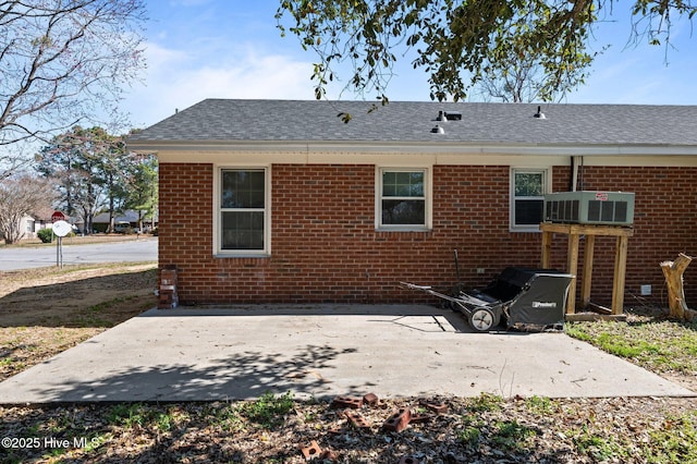 rear view of house with a shingled roof, a patio area, and brick siding