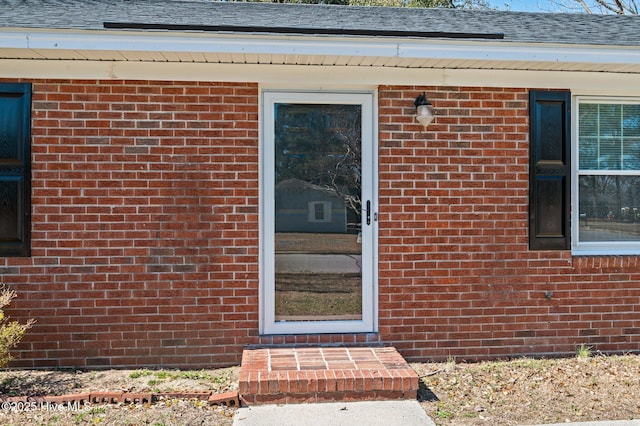 entrance to property featuring brick siding and roof with shingles