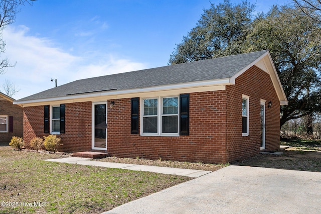 ranch-style home featuring a shingled roof, a front yard, and brick siding