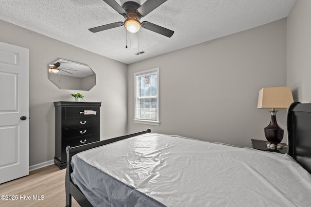 bedroom featuring baseboards, visible vents, light wood-style flooring, ceiling fan, and a textured ceiling