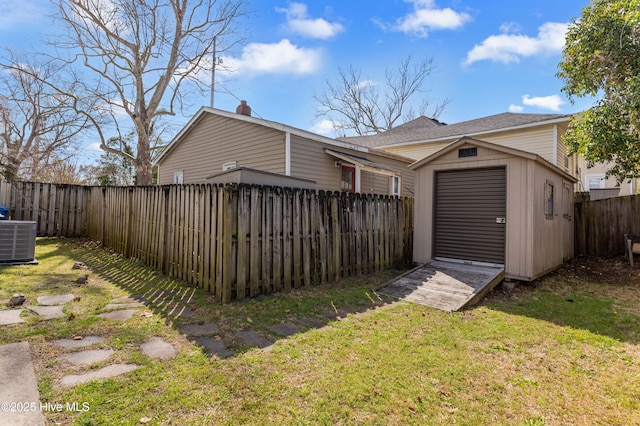 back of house featuring a fenced backyard, cooling unit, an outdoor structure, a lawn, and a storage unit