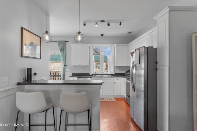 kitchen with dark countertops, stove, freestanding refrigerator, a peninsula, and white cabinetry