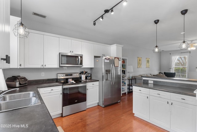 kitchen with appliances with stainless steel finishes, dark countertops, visible vents, and a sink