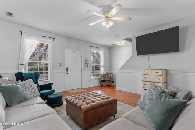 living area featuring ceiling fan, wainscoting, wood finished floors, and visible vents