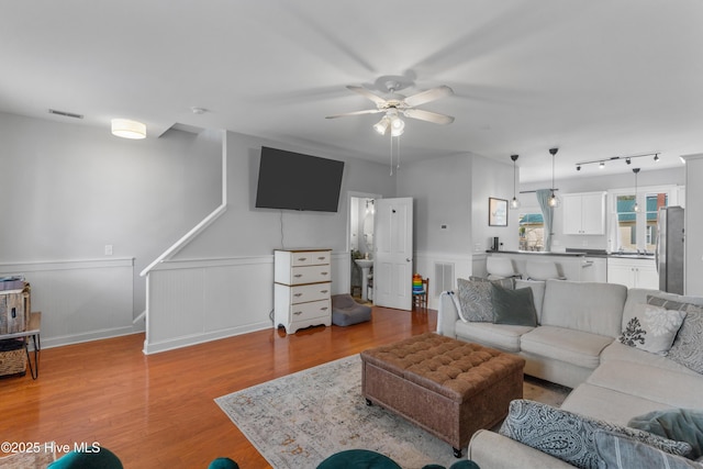 living area with a wainscoted wall, wood finished floors, visible vents, and a ceiling fan