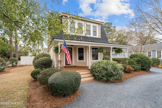 view of front of home with a shingled roof, covered porch, and fence