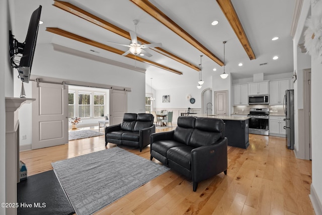 living area with vaulted ceiling with beams, a barn door, recessed lighting, light wood-style floors, and a ceiling fan