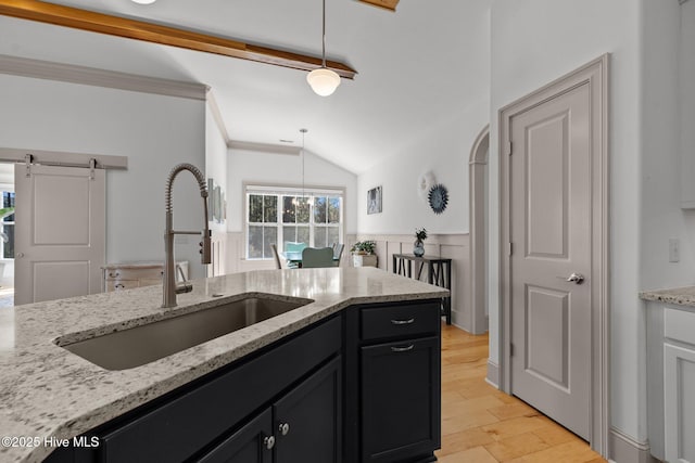 kitchen featuring pendant lighting, a sink, dark cabinetry, a barn door, and vaulted ceiling