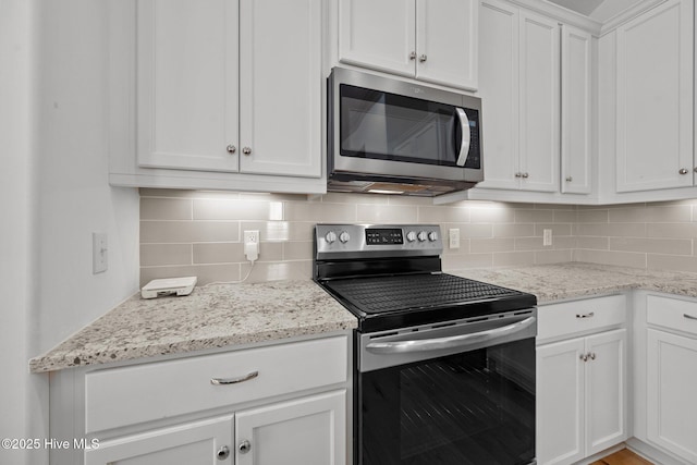 kitchen featuring backsplash, appliances with stainless steel finishes, white cabinetry, and light stone countertops