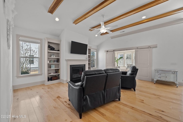 living area featuring a glass covered fireplace, plenty of natural light, light wood-type flooring, and vaulted ceiling with beams