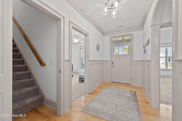 foyer with light wood-type flooring, a wainscoted wall, stairs, and crown molding