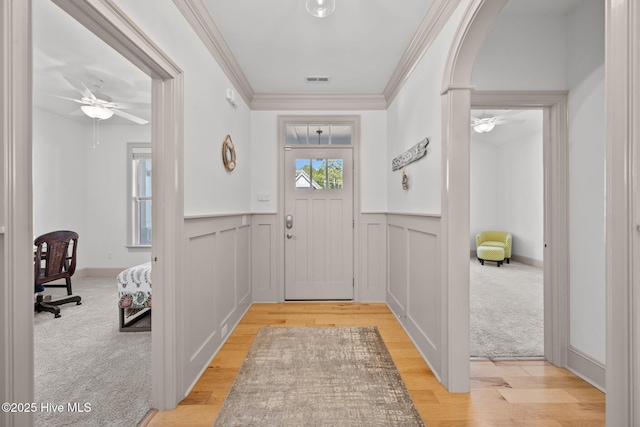 entryway featuring a wainscoted wall, a ceiling fan, light wood-type flooring, and ornamental molding