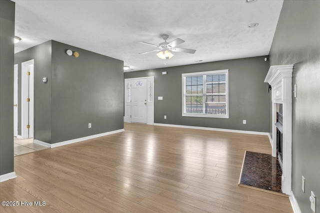 148 Mendover Dr, Jacksonville, NC 28546 - unfurnished living room featuring a fireplace with flush hearth, ceiling fan, light wood finished floors, baseboards, and a textured ceiling