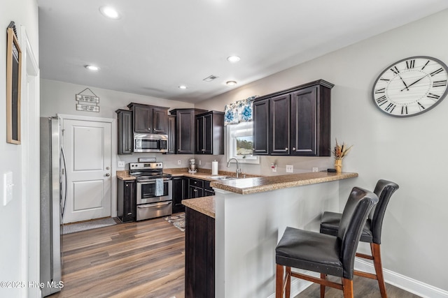 kitchen featuring dark wood finished floors, appliances with stainless steel finishes, a sink, a peninsula, and a kitchen breakfast bar