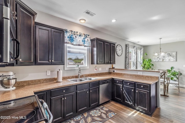 kitchen featuring light wood finished floors, visible vents, appliances with stainless steel finishes, a peninsula, and a sink