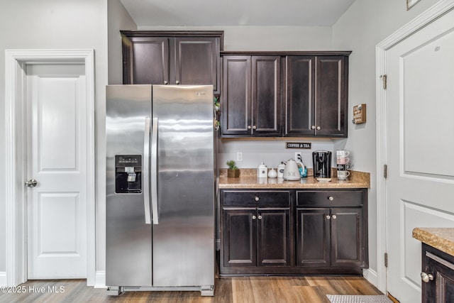 kitchen with dark brown cabinets, light stone counters, stainless steel fridge, and light wood-style flooring