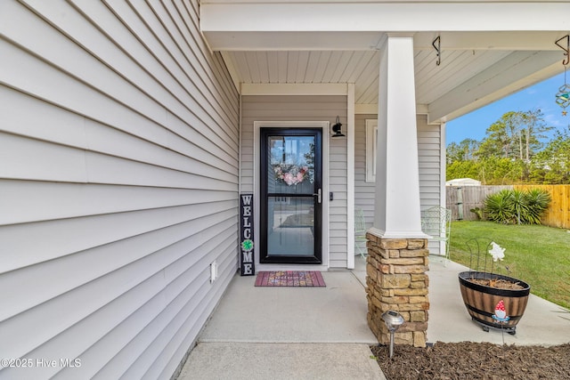 entrance to property featuring stone siding, fence, and a lawn