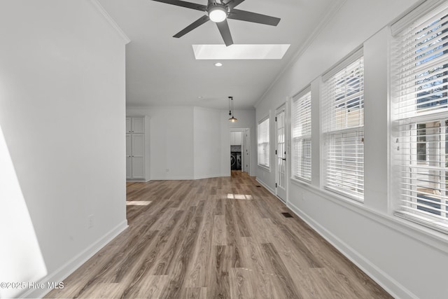 interior space with a skylight, baseboards, crown molding, and wood finished floors